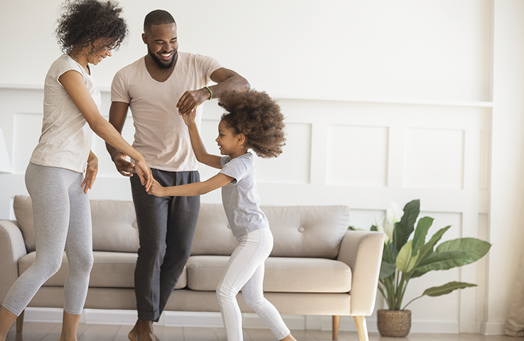 Happy african American young parents dance with cute little preschooler daughter in living room, smiling loving family with small kid have fun playing together at home, enagaged in physical activity